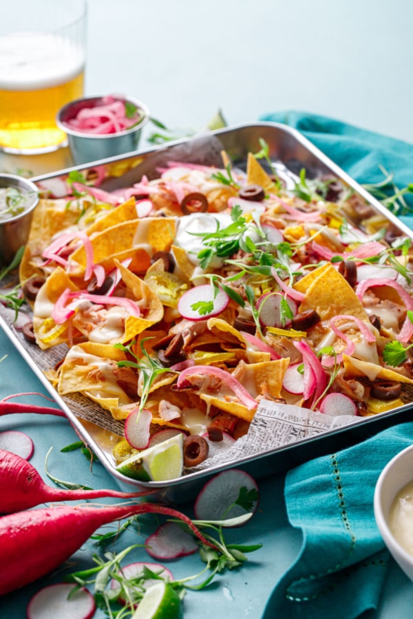 Sheet pan of Loaded Smoked Chicken Nachos with a glass of light beer in the background