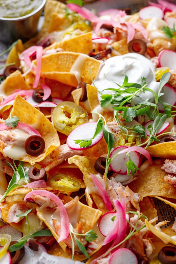 Closeup, Loaded Smoked Chicken Nachos topped with sour cream, cilantro, radishes and pickled onions