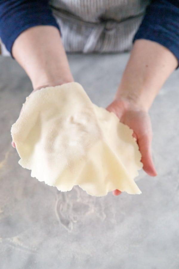 Hands holding a piece of super thinly rolled semolina cracker dough, showing just how thin the dough is.