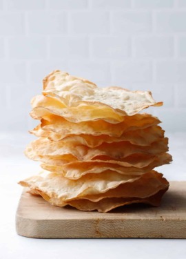 Side view stack showing just how thin and crispy these semolina sourdough crackers are, stack sitting on a distressed wooden bread board.
