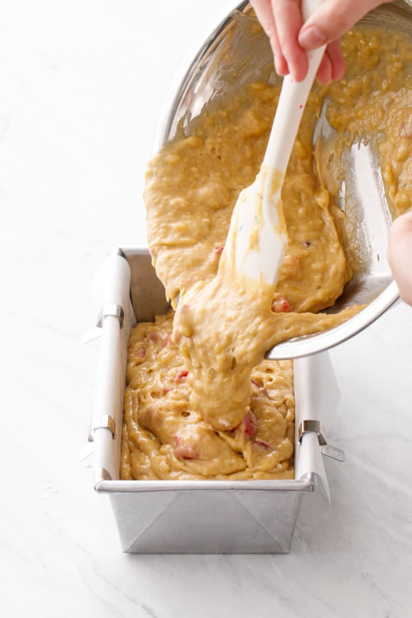 Pouring the strawberry banana bread batter into a parchment-lined loaf pan.