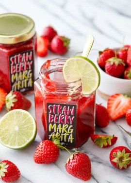 Homemade strawberry margarita jam in hexagon glass jars with custom designed labels, surrounded by fresh strawberries and limes.