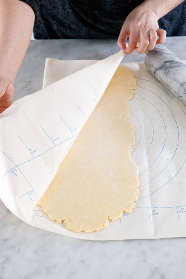 Rolling pie dough folded inside a pastry cloth to form a rectangular shape.