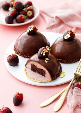 Dome-shaped strawberry mousse cakes, three on a white plate, one sliced to show the brownie inside