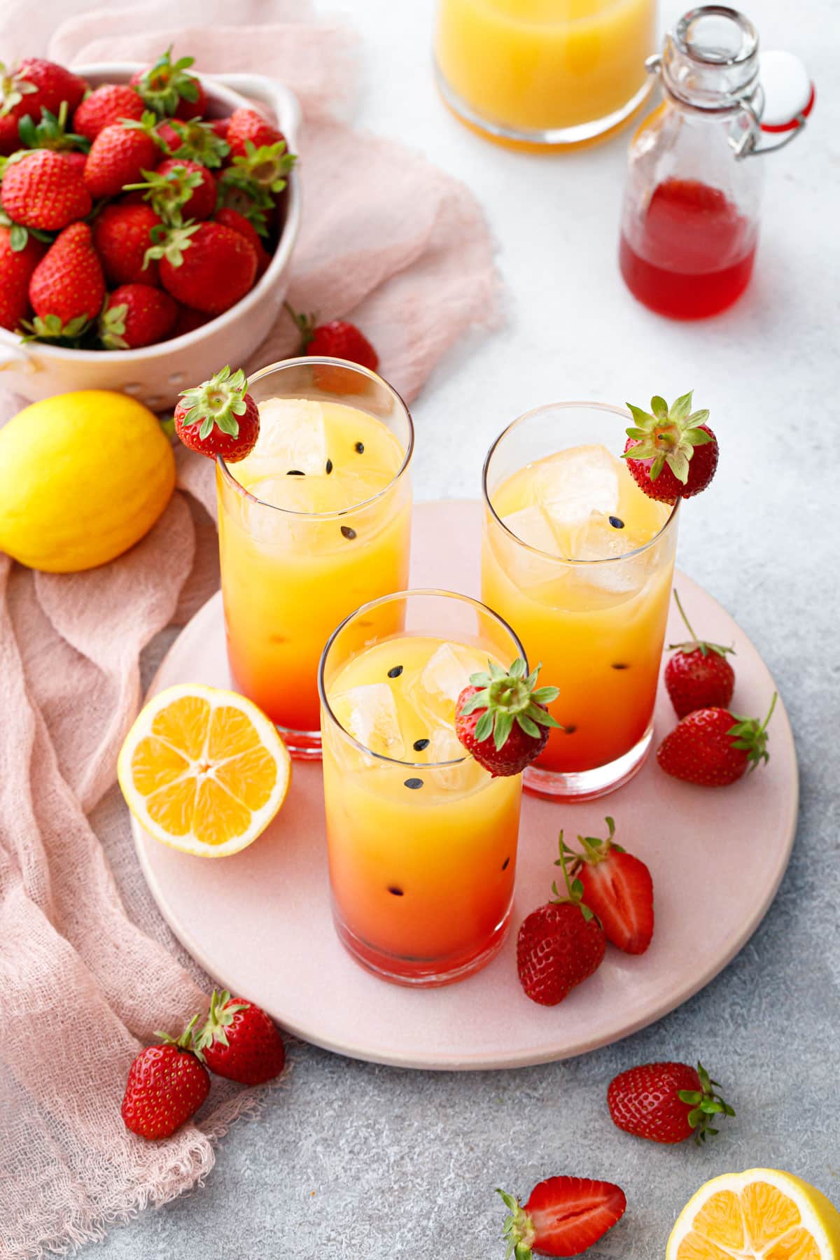 Three glasses of Strawberry Passionfruit Lemonade, colored with a gradient red to yellow with black passionfruit seeds.