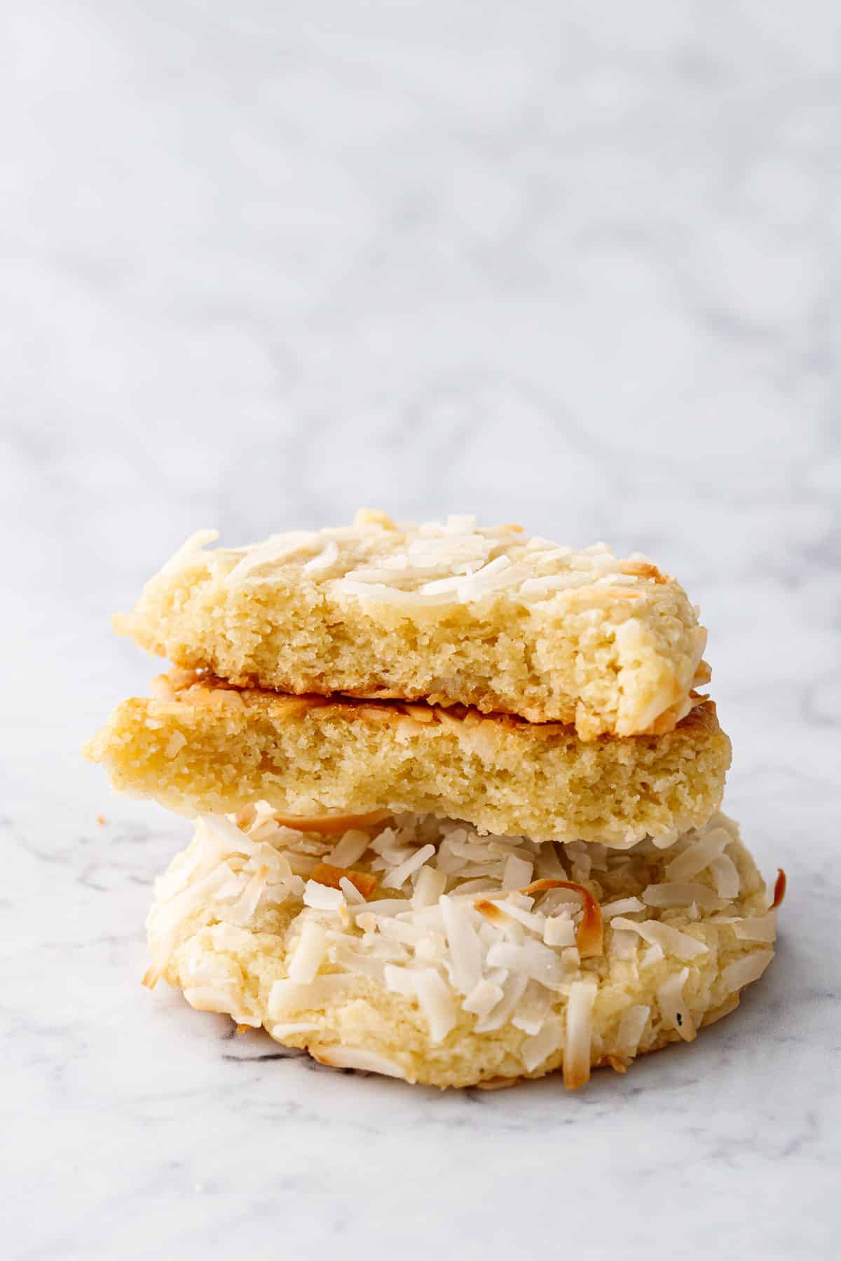 Stacked Toasted Coconut Sugar Cookies, one cookie broken in half to show the soft and chewy interior texture.
