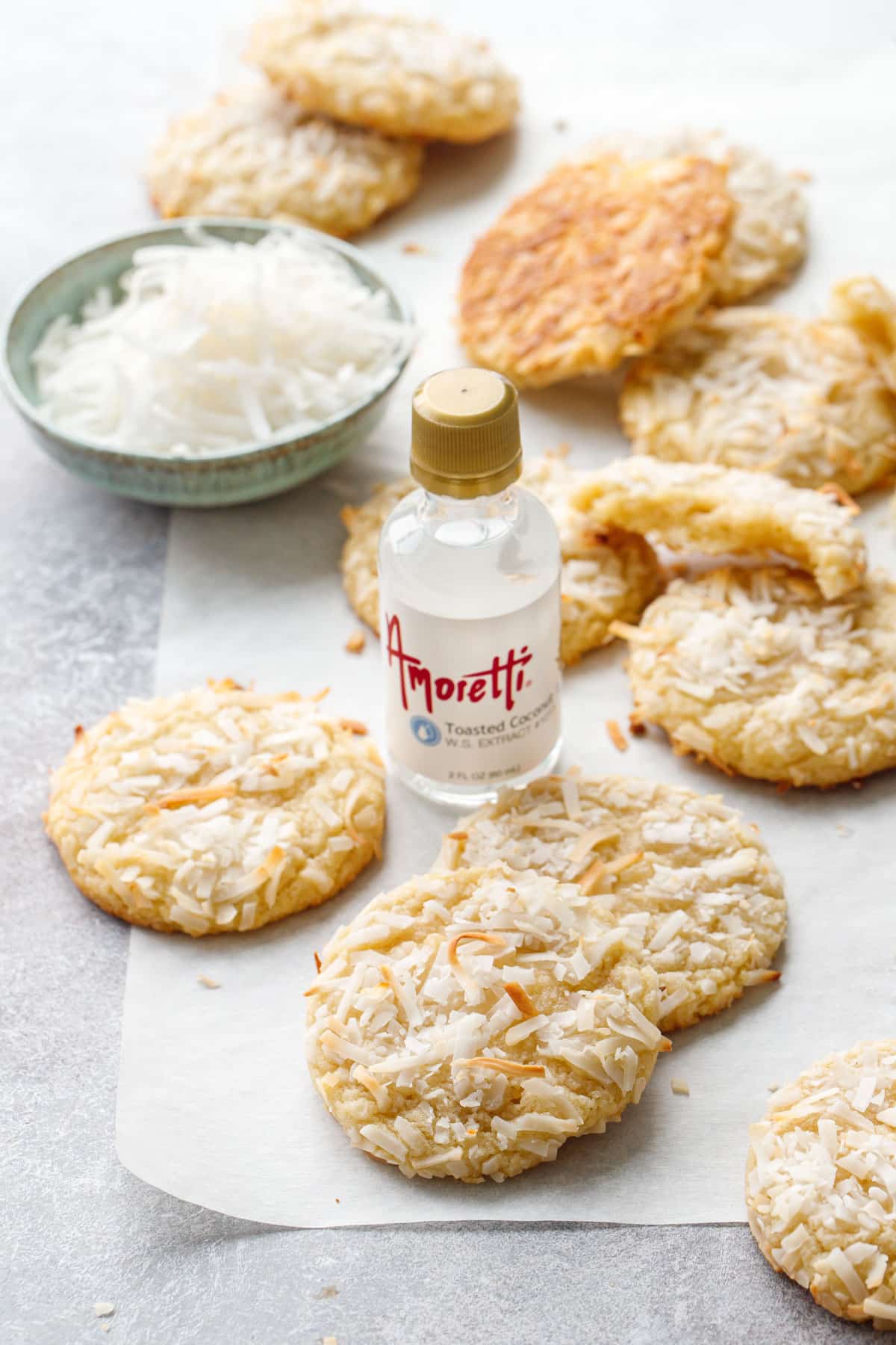 Toasted Coconut Sugar Cookies scattered on a piece of parchment, with bottle of Amoretti coconut extract in the middle.