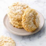 Stack of Toasted Coconut Sugar Cookies on a plate with one cookie leaning up against the stack to show the toasted shredded coconut on top of the cookie.