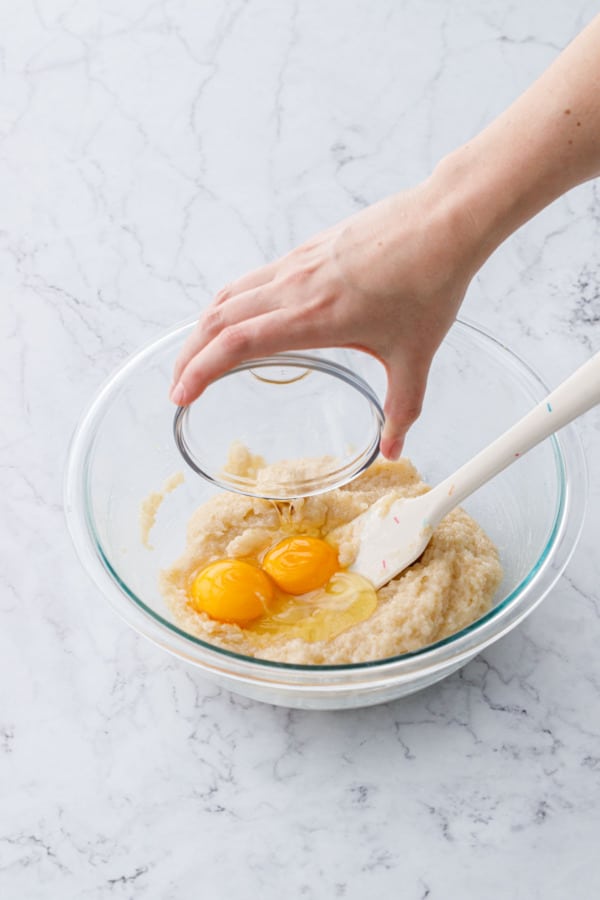 Pouring egg and egg yolk into mixed ingredients in a glass mixing bowl.