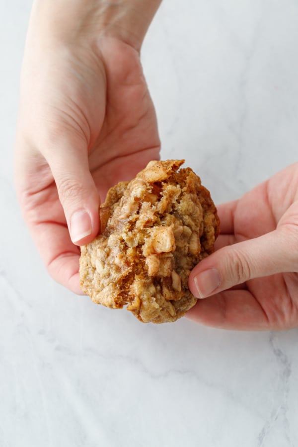 Hands breaking a Toffee Apple Oatmeal Cookies in half to show the chewy texture in the middle