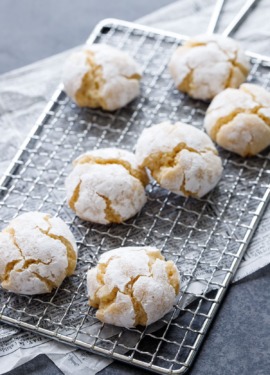 Powdered-sugar coated crinkle cookies on a wire rack, on newsprint parchment on a dark background.