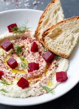 Closeup of white bowl with Whipped Almond Dip, topped with Pickled Beets, fresh dill and two slices of Sourdough