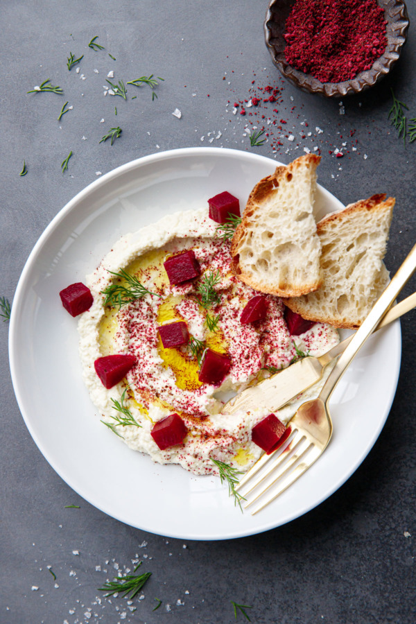 Overhead white bowl with a swirl of whipped almond dip, drizzled with olive oil and topped with cubes of pickled beets and fresh dill.