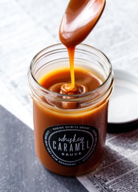 A spoon drizzling homemade whiskey caramel sauce into a jar full of caramel